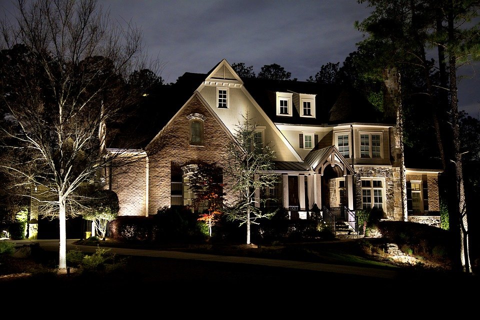 Large stone home dramatically illuminated with landscape up-lighting at night by Elegant Landscaping in Erie PA